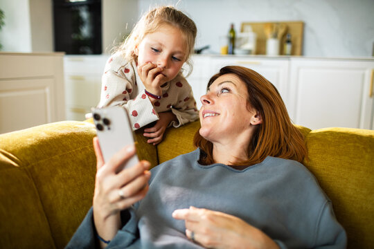 Mother and daughter using smartphone on sofa at home
