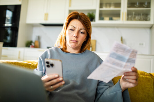 Concerned woman reviewing household bills on smartphone at home