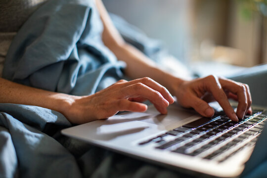 Person typing on laptop in bed at home