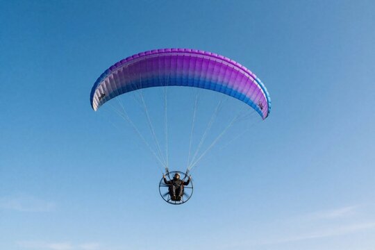 Motoparaplan pilot flies solo against clear blue sky. Single man controls purple paraglider wing with motor engine in air. Extreme sport adventure, paramotor flight, gliding activity, feeling