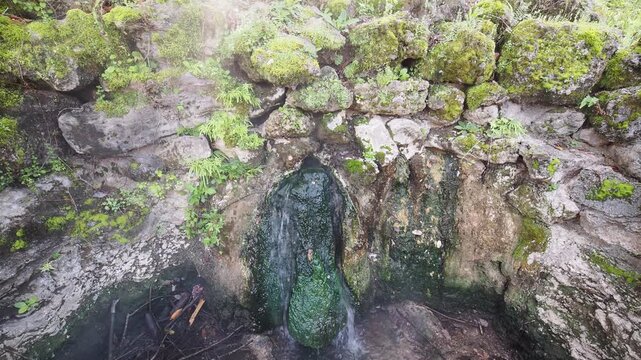 Water flowing from moss covered stone wall.