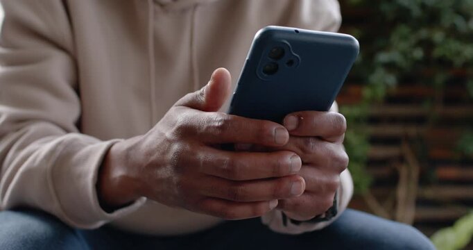 African American man tapping and scrolling blue phone with wristwatch on bench, reacting to message