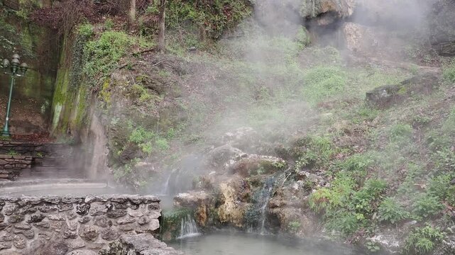 Steam rising from hot spring water in forested rocky terrain.