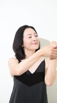 腕を手でケアする50代女性、エイジングケアと日焼け止めやスキンケアやリンパのマッサージをするミドル世代の美容イメージの縦動画