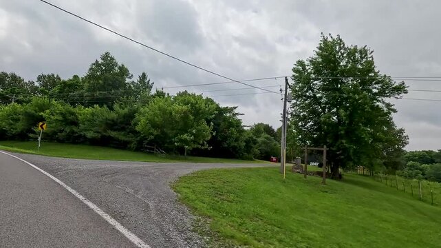 Driving POV traveling down a winding country road in Southern Illinois. Features sharp curves, lush green fields, and roadside trees under summer skies.