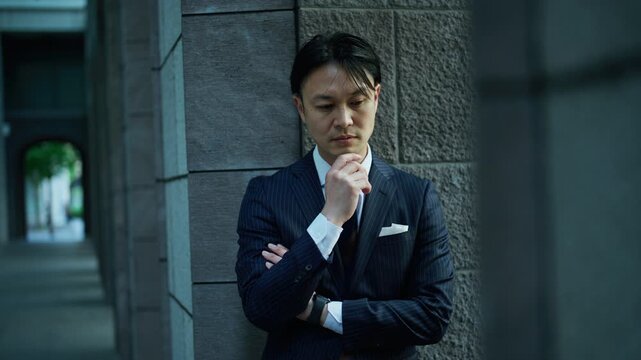 Japanese businessman deep in thought beside a dark stone wall