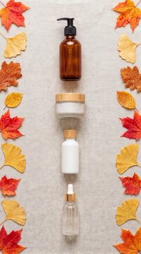 Autumn flat lay composition with organic cosmetic bottles aligned in the center and framed by colorful fall leaves on linen background, seasonal natural skincare concept
