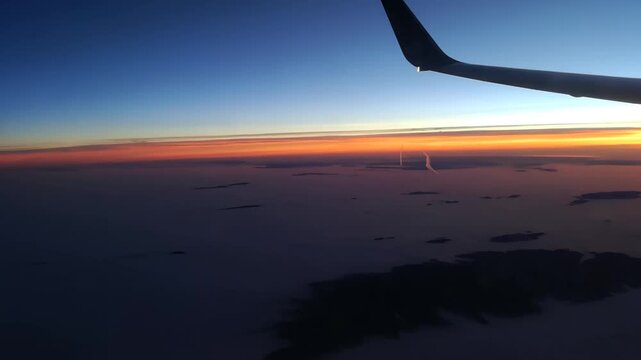 Airplane wing view during sunset flight above clouds with vibrant orange and blue sky gradient