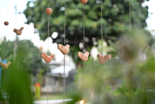 hanging handcrafted terracotta bird mobiles on strings with blurred garden foliage, rustic luxury brazilian event decoration, selective focus vertical shot