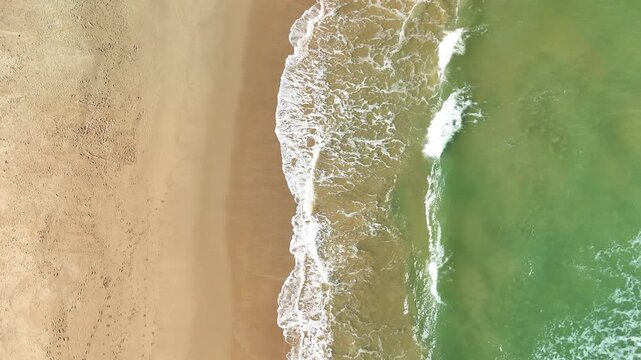 White sea waves gently roll toward a sandy beach, creating a peaceful coastal landscape. Ideal for themes of nature, ocean, travel, summer vacation, relaxation, and tropical destinations.