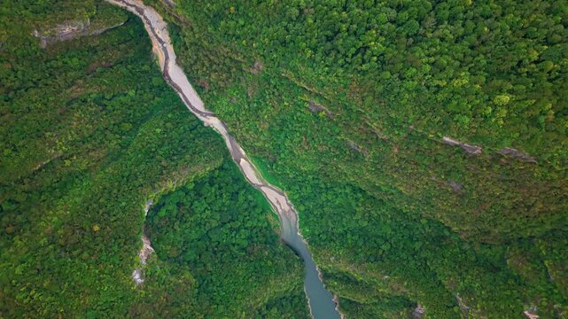 Aerial forward descend over a winding dry riverbed and lush canyon forest on an overcast day. Scenic nature establishing shot for environmental, geology, and travel documentary projects.