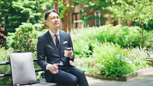 Businessman resting with a takeaway coffee beside a green planting