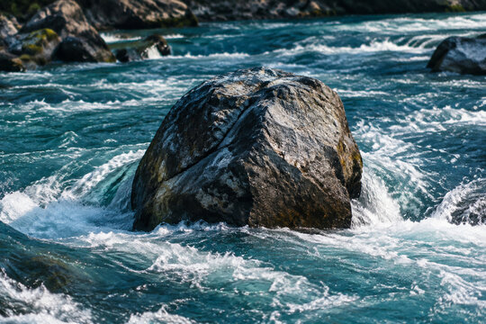 A large boulder standing in the center of a fast-flowing mountain river.