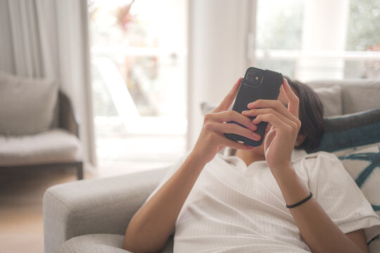 smartphone, teenager, using phone, lifestyle, sofa, home, communication. young person lying on a couch browsing social media and texting on a mobile device in a bright living room.