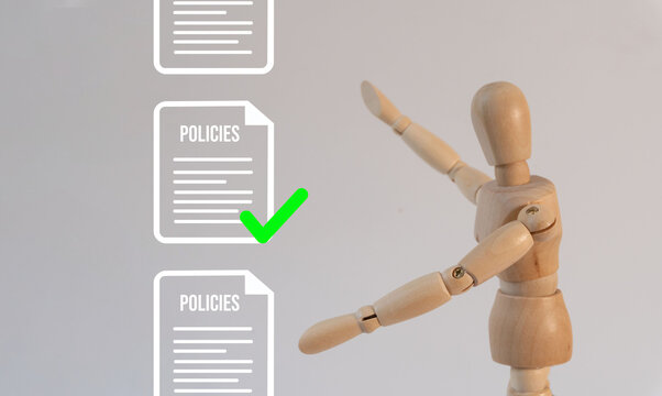 Wooden mannequin points at checked document labeled 'POLICIES'. Image symbolizes approval, compliance, or policy implementation. Suitable for corporate, legal, or training materials