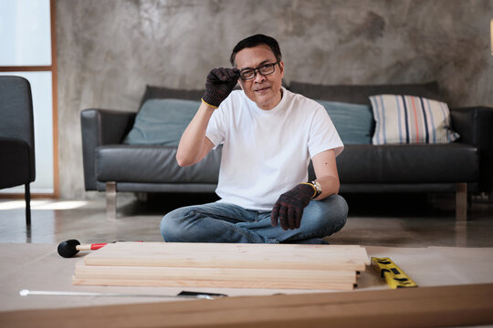 Portrait of Asian mature man preparing flat-pack furniture parts, cheerful smile, self-assembly with carpentry diy tools, home improvement, craft install hobby workshop, handyman active lifestyle.