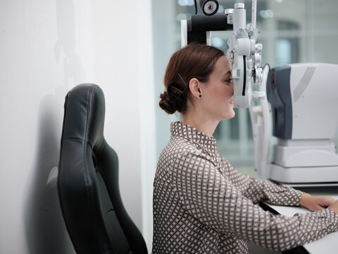 White female patient eye exam with phoropter equipment, vision and eyesight improvement by expert optometrist woman, diagnostic for eyeglasses lens, professional technology services in optical clinic.