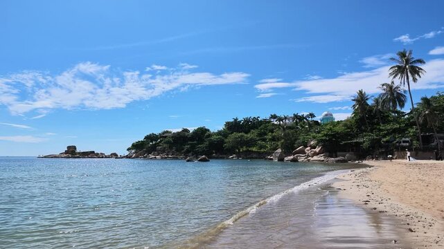 Wide establishing shot of a calm tropical ocean beach with a green island on the horizon.