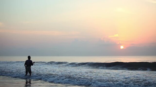 Silhouette of Fisherman Casting Net into Ocean Waves at Sunrise