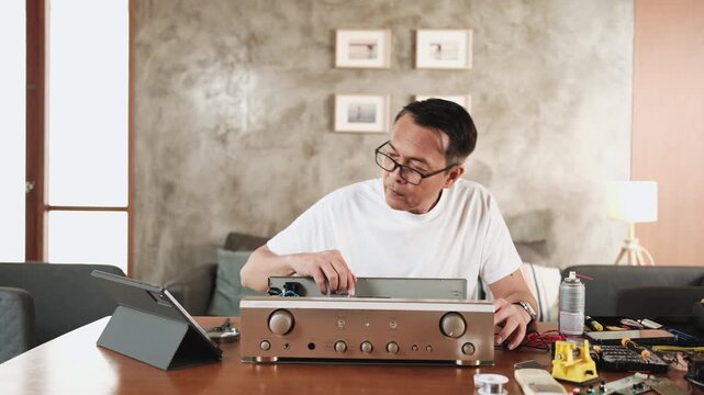 Mature Asian man disassembling audio equipment and self-learning, searching for manual guide to fix circuit board in tablet, home appliance DIY, electronics component hobby, handyman skill workshop.