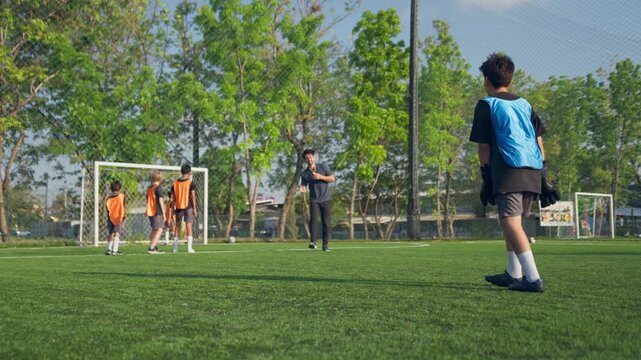 Caucasian male coach teaching kid football team on outdoor sports field. 