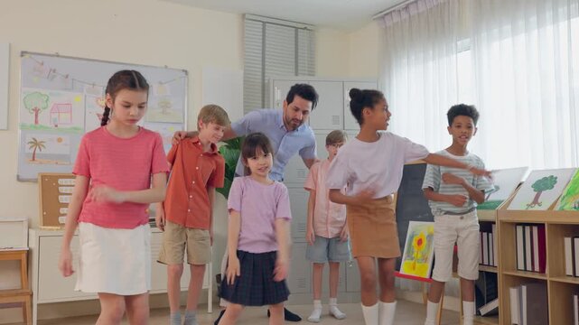 Diverse students dancing with male teacher in classroom at elementary school. 