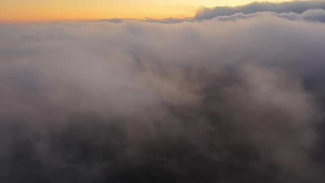 Sunset glows through drifting clouds above. Clouds roll softly, casting dark shadows below in Indonesia