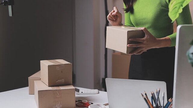 Close up with Start up small business, SME female owner using laptop checking order online to prepare to pack a box of goods for sale to customers, sme business idea.