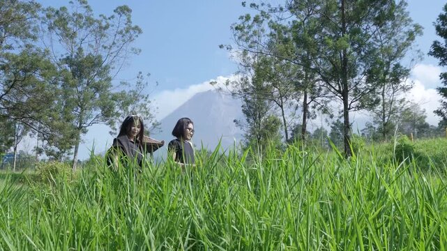 Two Women Exploring a Green Mountain Landscape with Mount Merapi View