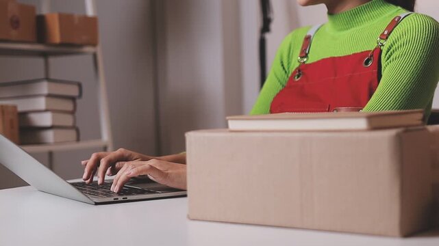 Close up with Start up small business, SME female owner using laptop checking order online to prepare to pack a box of goods for sale to customers, sme business idea.