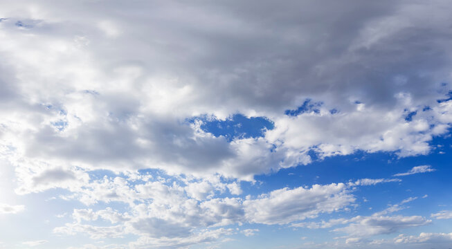 A daytime sky scene with thick gray clouds overlapping bright blue clear sky, showing a mix of overcast and open areas.