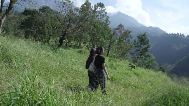 Two Women Hiking Through Green Hills at Kali Talang with Mount Merapi View