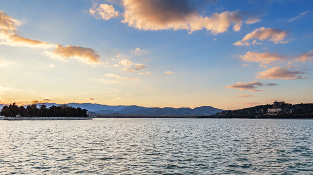 A calm lake landscape at sunset, with distant mountains and soft clouds in the sky.