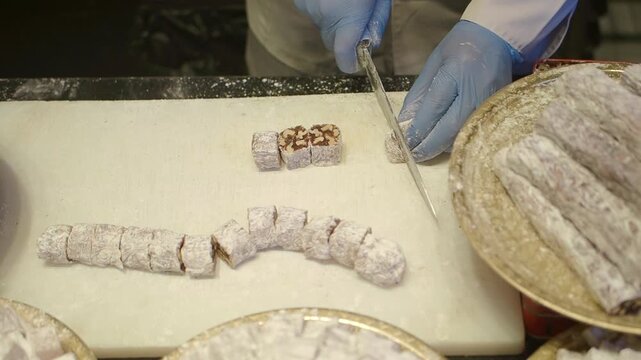 A person cuts turkish delight on a counter while customers look on in a busy shop