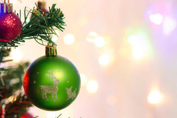 Fototapeta premium Green bauble ornament hanging on evergreen Christmas tree branch with red decoration sphere, surrounded by glowing holiday light creating joyful cheerful festive mood