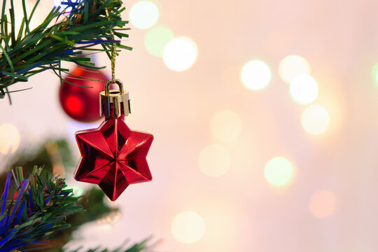 Red star ornament decoration hanging on green christmas tree branch with soft bokeh light creates festive holiday atmosphere full of joyful mood and winter celebration