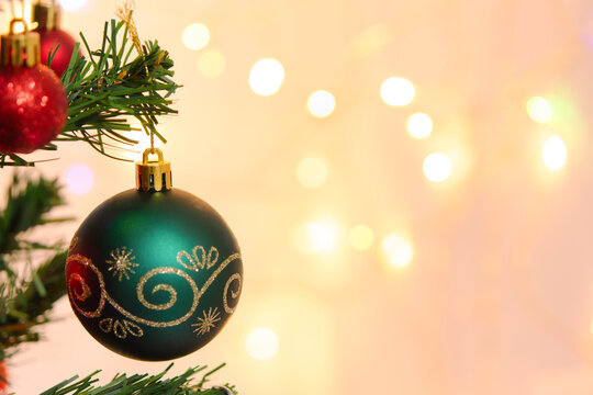Joyful green bauble hanging on pine tree branch with shiny red ornament decoration, warm soft bokeh light glow, creating festive christmas holiday mood