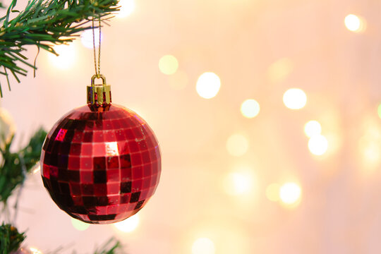 Red christmas tree ornament bauble hanging on green pine branch brings festive joy, holiday cheer, sparkling bokeh light background creating warm magical feeling