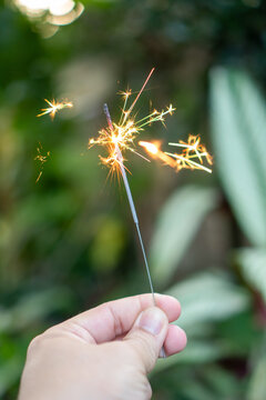 Hand holding glowing sparkler outdoor in lush garden brings pure joy, bright light, and festive excitement during an evening celebration with magical sparks