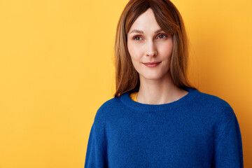 Fototapeta premium Cheerful woman portrait, smiling softly, blue sweater against warm yellow background, natural lighting, relaxed pose, clean colors, simple studio setting and contemporary vibe