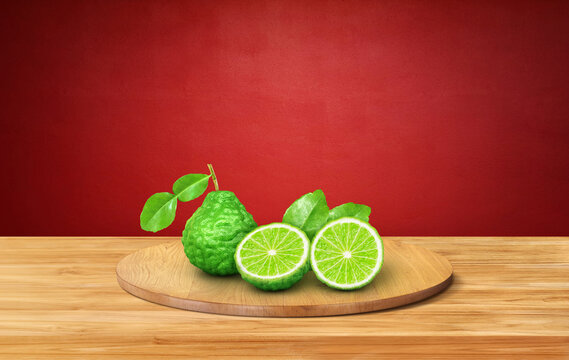 Whole and halved bergamot fruits with leaves on round wooden platter.
