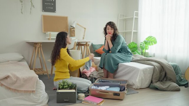 Latino mother helping young daughter unpack suitcases in university dormitory.