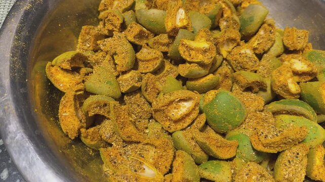 Camera orbiting around a bowl of raw mango pieces coated in a dry spice blend during traditional Indian pickle preparation