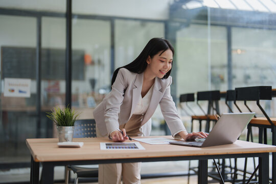 Businesswoman standing at desk using laptop reviewing documents