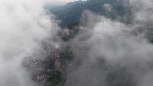 Misty drone shot of tropical mountain ridge with telecom towers emerging through low clouds.