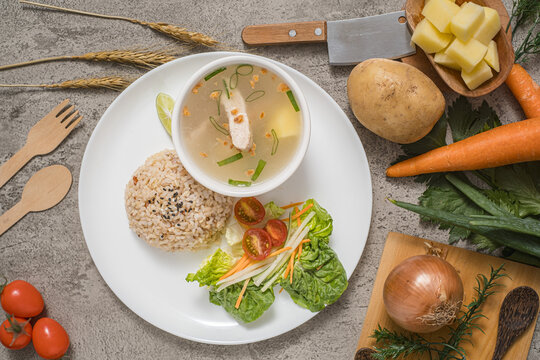 Original chicken soup served in a bowl, accompanied by red rice, citrus slices, and a side salad arranged on a plate, complete with fresh ingredients used as props.