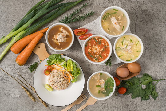 Red rice and a side salad arranged on a plate, accompanied by various types of soup and fresh ingredients used as props.