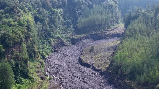 High altitude wide panorama of an expansive, barren volcanic lava canyon left dehydrated below the peak of Mount Semeru.