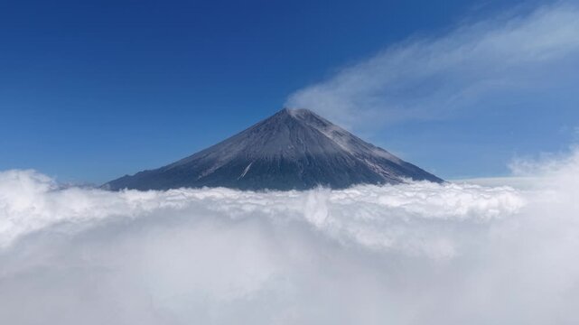 Dramatic Mount Semeru peak rising through dense cloud inversion under vivid blue sky.