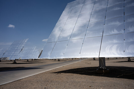 giant parabolic solar concentrator mirrors in desert landscape under blue sky